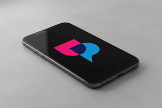 UpScrolled logo in pink and blue speech bubble design on smartphone screen against neutral gray background.