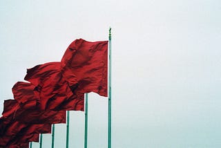 Five red flags blowing left on flagpoles.