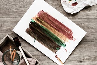 An abstract rendering of a rainbow, painted in dark colours on a white piece of paper.