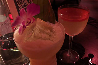 A large yellow drink garnished with an orchid and a smaller, clear drink