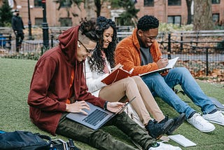 Three students laughing on a university campus lawn