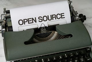 A typewriter with the words open source printed on the paper that is being fed through it.