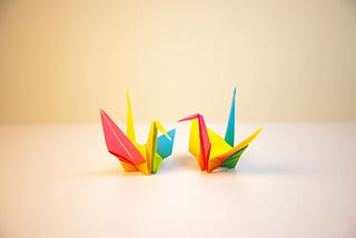 Two origami cranes made out of brightly covered paper sit on a table facing each other.