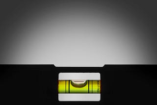 A black carpenter’s level against an illuminated grey background, will yellow liquid in the glass tube and the air bubble centered between the measuring lines.