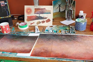 Orangutan matter studio behind the scene photo of a wooden table with background paintings of Unleaving. the paintings color show that even the warm backgrounds tend to be on the nuetral side of things.