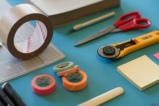 Tape, rotary cutter, notes, and scissors on a blue desktop