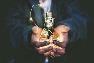 A person holding an illuminated light bulb.
