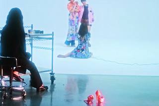 Limi, the main character of “Followers,” is sitting barefooted while taking photos of the two models in a studio, while her high heels are lying behind her.