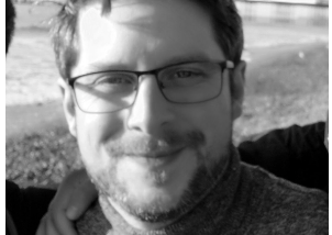 A black and white photo of Rory, a white man with glasses wearing a polo neck jumper.