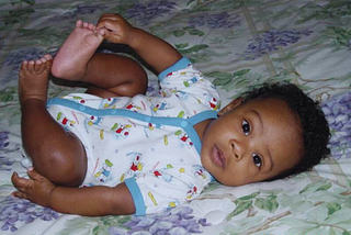 My one month old baby laying on my bed, staring back at the camera holding one toe mid air — as tiny and helpless as can be — yet tranquil