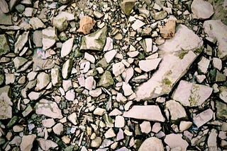 view looking down on a rocky shoreline, scattered rocks of different shapes and sizes and my two feet in the middle