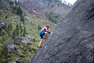 Man climbing rock face, with safety rope belay connection.