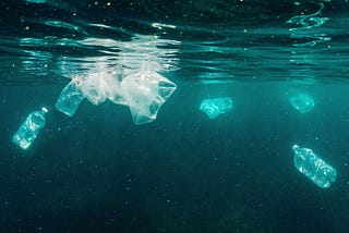 Resíduos plásticos flutuando e submersos no oceano, incluindo garrafas e sacolas transparentes, evidenciando a poluição marinha em águas azul-esverdeadas