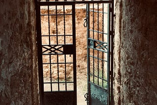 Iron doorway halfway open leading to an earthen wall. Taken in Lanjaron, Spain