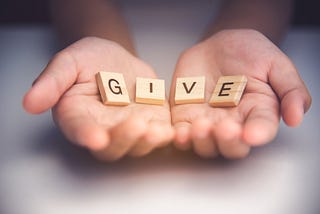 Cuppted hands holding wooden tiles that spell the word “GIVE”