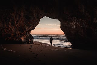 Man standing in front of a beach cave entrance