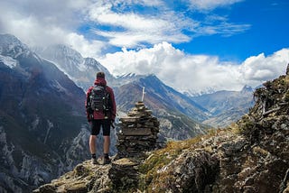 man on a hike in front of a stone pile, maybe a grave, in the mountains. What do you control?