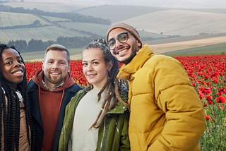 A group of friends smiling with autumn coats in front of a poppy field.