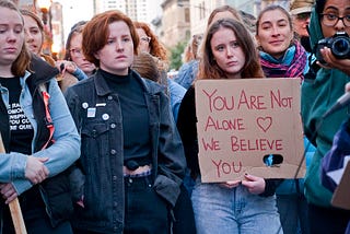 A group of students gathers to speak up for sexual violence survivors. One student is holding a sign that reads ‘You are not alone. We believe you.”