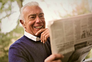 smiling mature man wearing dark sweater reading newspaper