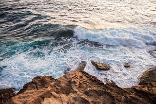 Colour image of rocks at a cliff base and ocean waves crashing onto them