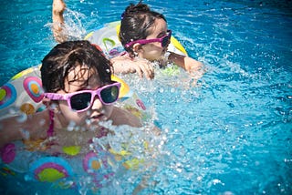 Two little girls in a swimming pool, with inner tubes and pink sunglasses