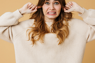 Girl with finger plugging up both her ears and a grimace on her face indicating she doesn’t like the noise.