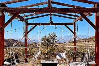 A set of swings installed from a wooden structure with a stone fireplace in the middle, with a view of the valley.