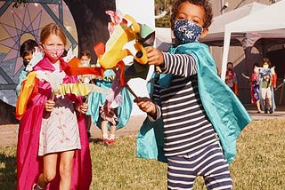 Two children wearing masks and capes playing outdoors at school