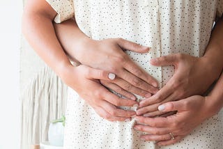 Man’s hands hugging the pregnant belly of a woman from behind