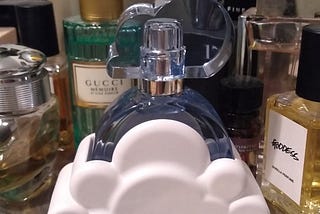 a bottle of Ariana Grande’s Cloud perfume, surrounded by various other perfume bottles, resting on a silver dish.