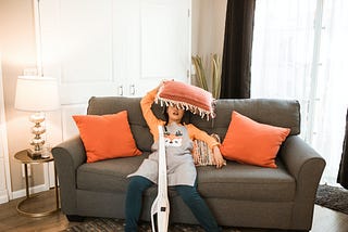 woman, exhausted from vacuuming, collapses on a grey couch with orange throw cushions.