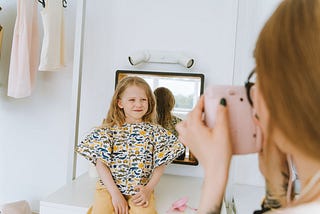A mother photographs her smiling daughter indoors, capturing a joyful moment.