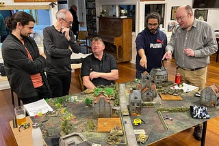 Image of a wargame setup on a table with gamers interacting.