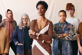 Group of diverse women standing confidently together against a neutral background, representing leadership, clarity, and collective strength in design and tech.