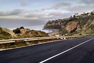 Color photo of road leading down to the Pacific Ocean cloudy sky above ocean and bluffs of Palos Verdes Peninsula in the background to the right Stella Martann copyright 2019.