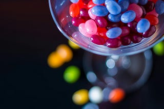 Colourful candy beans falling out of a glass utensil