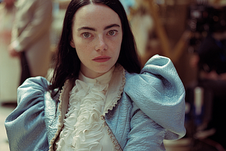 Bella Baxter (Emma Stone), a pale, white woman with black hair and blue eyes, wearing a dress with puffy sleeves in Poor Things.