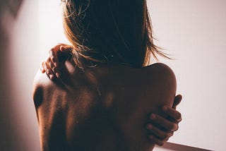A picture of the back of a naked woman hugging herself as if exposed