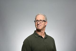 A head and shoulders shot of a white man with greying hair and glasses standing tall and looking somewhat proud of himself.