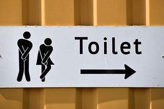 A toilet sign with a symbol of a man and woman crossing their legs.