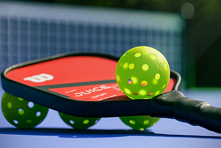 Pickleball paddle and balls, sitting on a pickleball court.