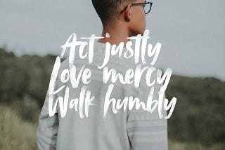 A young person with brown skin and glasses wearing a grey sweater faces away from the viewer. Text in the foreground reads, “Act justly; Love mercy; Walk humbly. Micah 6:8”