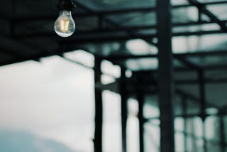 Dim light hanging in glass structure, with view of overcast sky.