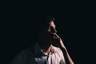 A young man with a white shirt thinking in a dark room