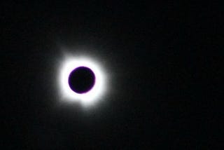 The circle of the sun eclipsed by the moon over a black background with bright rays of light around it.