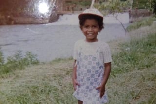 menina negra de quatro anos na beira de lago, sorrindo para a foto