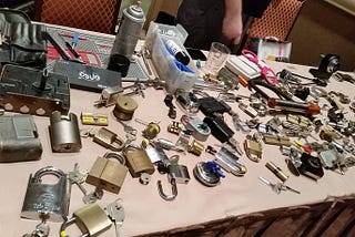 Beige Table covered in a variety of padlocks, lock cylinders, and lock picking tools.