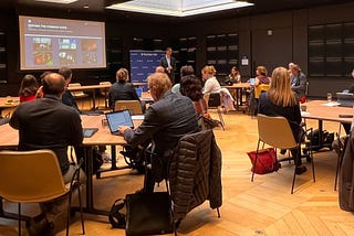 Room with round tables and attendees around them looking towards a screen and speaker Stefaan Verhuslt from The Data Tank standing next to the screen facing the room