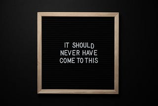 a white text on a black chalkboard with bronze borders, saying “It should never have come down to this.”